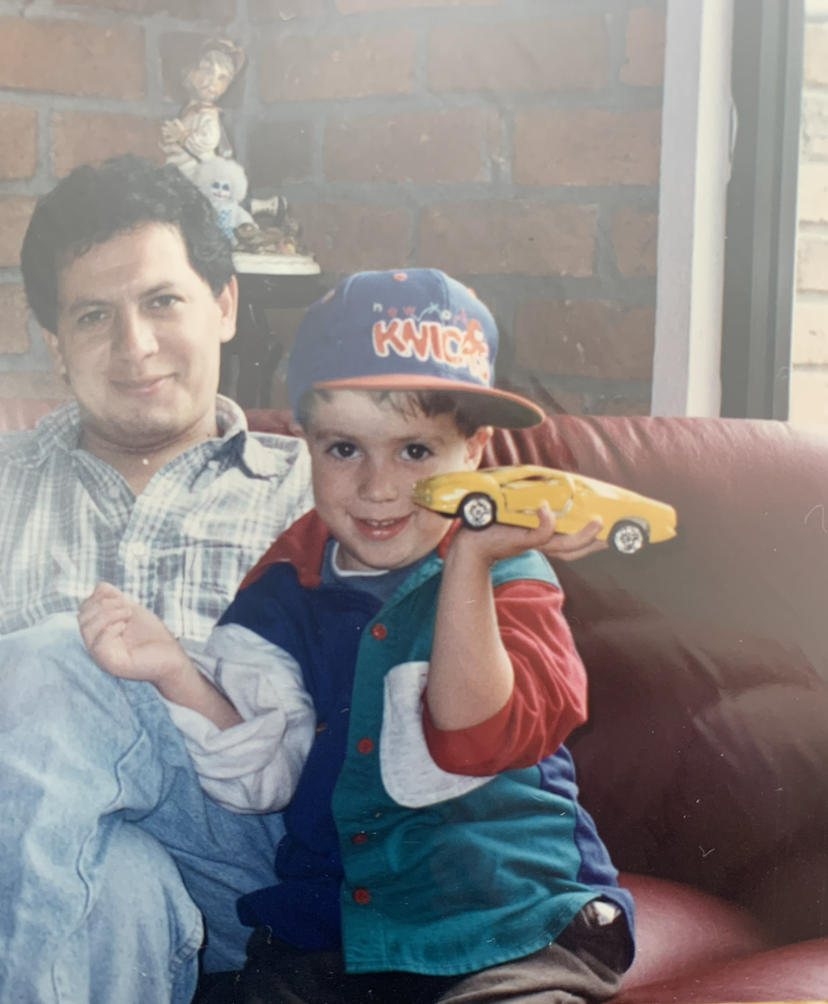 Young Jose holding a yellow toy car with his father, representing his lifelong passion for automobiles